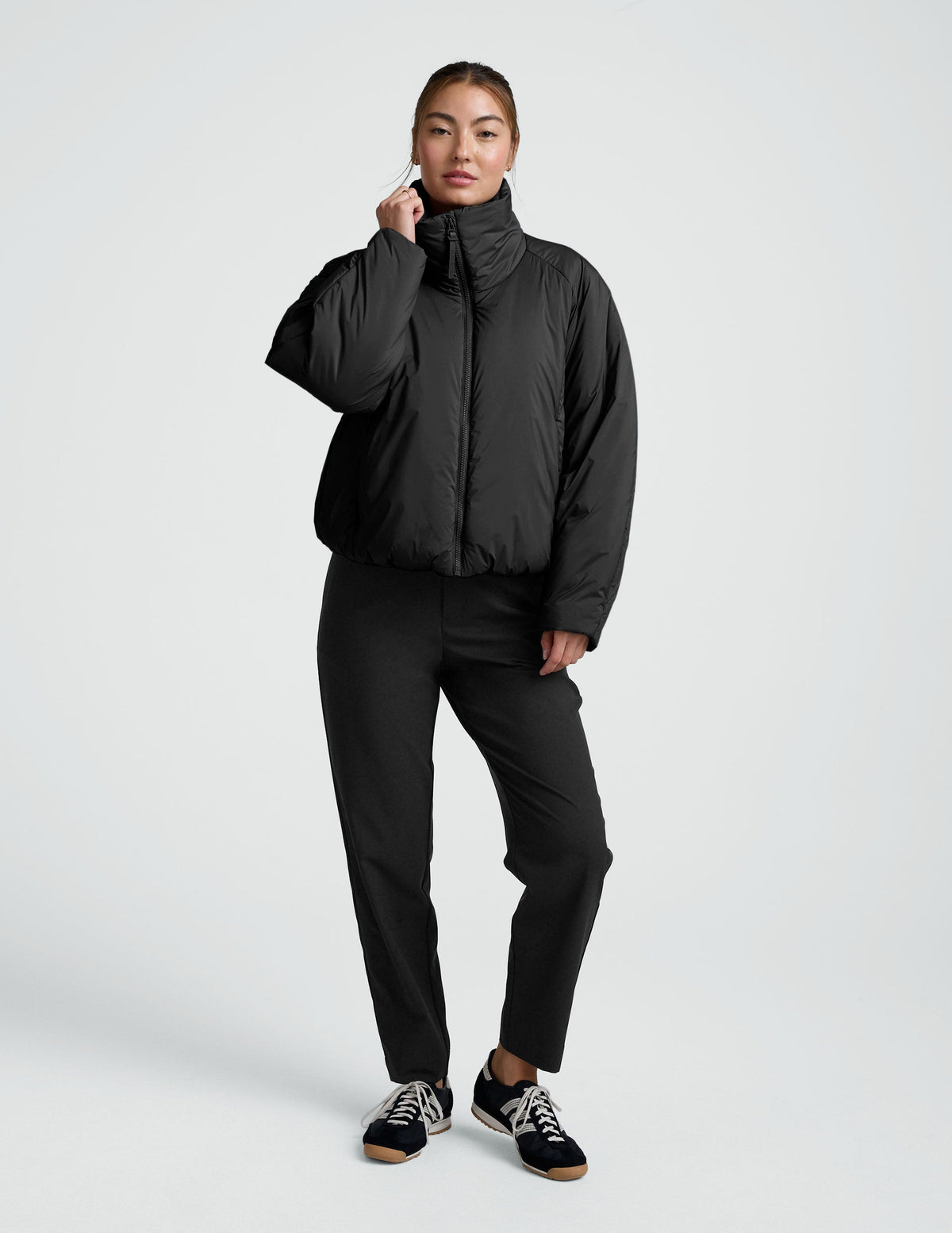 Person wearing a black zip-up puffer jacket and pants on a plain background.