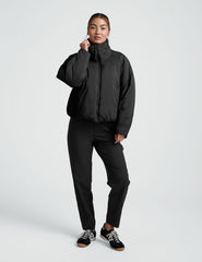 Person wearing a black zip-up puffer jacket and pants on a plain background.