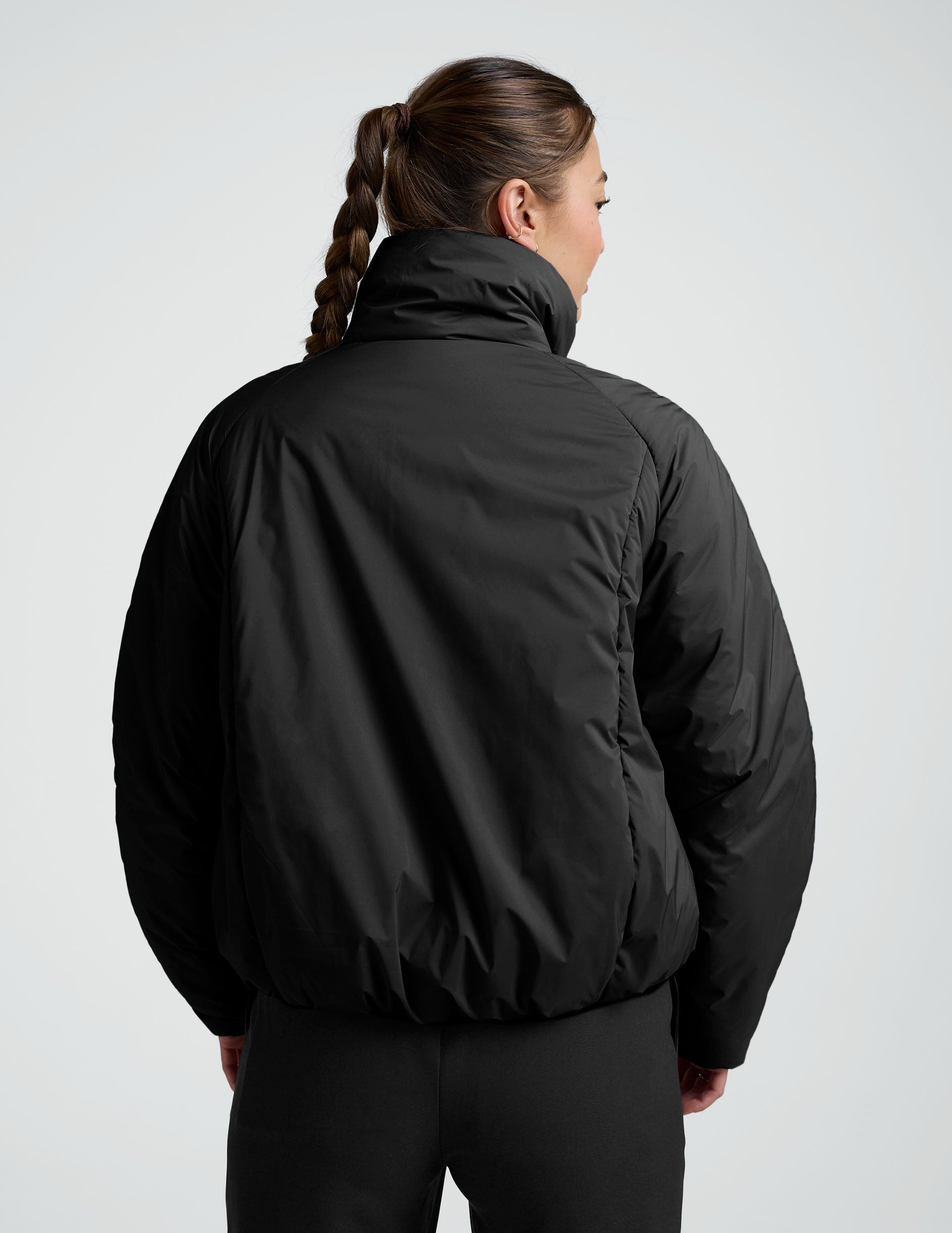 Person wearing a black zip-up puffer jacket and pants on a plain background.