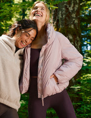 Two women laughing outdoors with a green forest background.