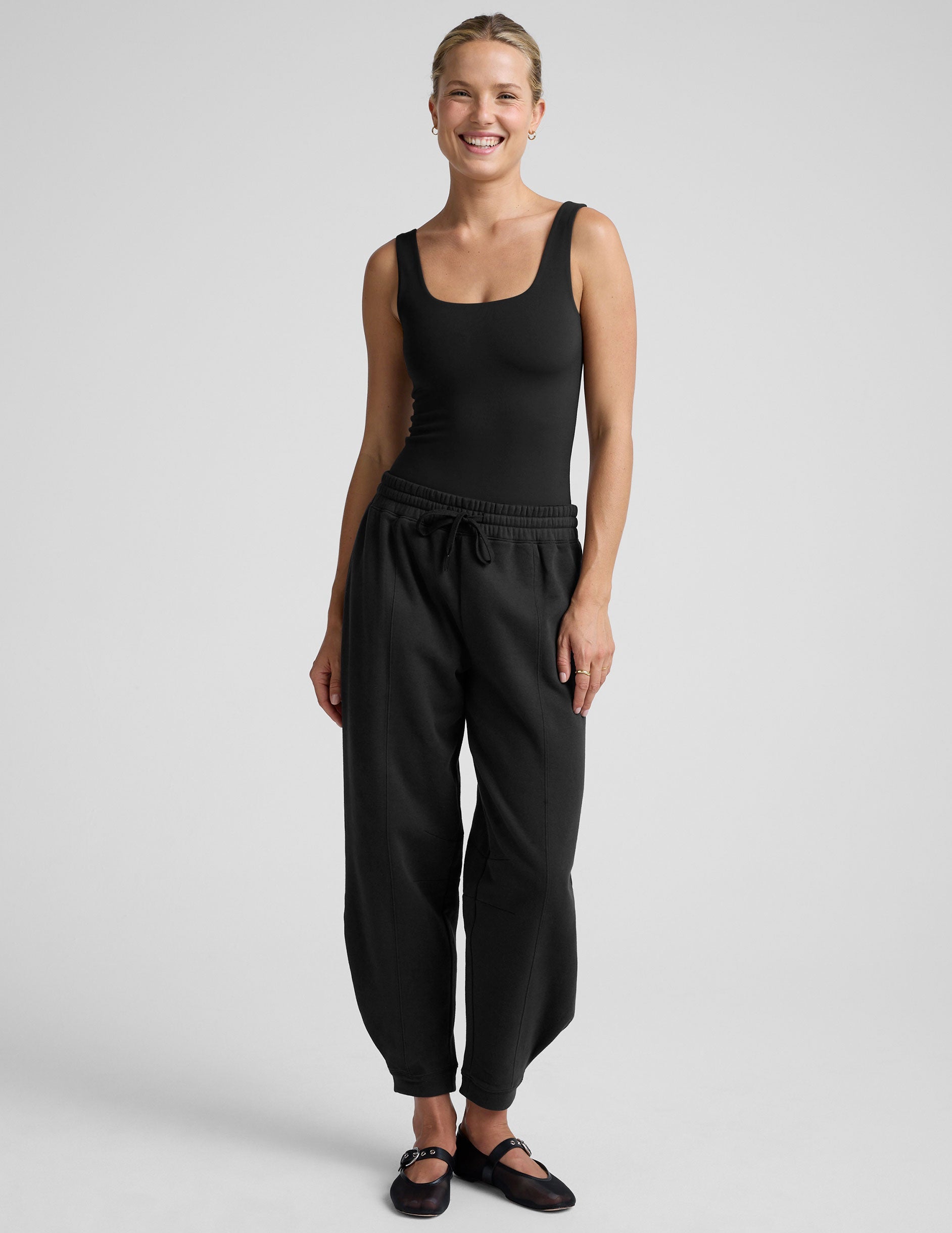woman wearing a black tank bodysuit and black pants against a plain background.