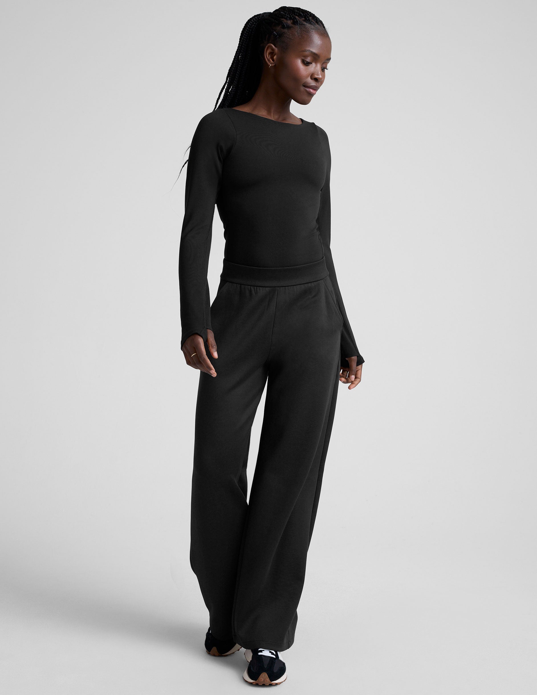 woman wearing a black long-sleeve boatneck bodysuit and black pants on a plain background.
