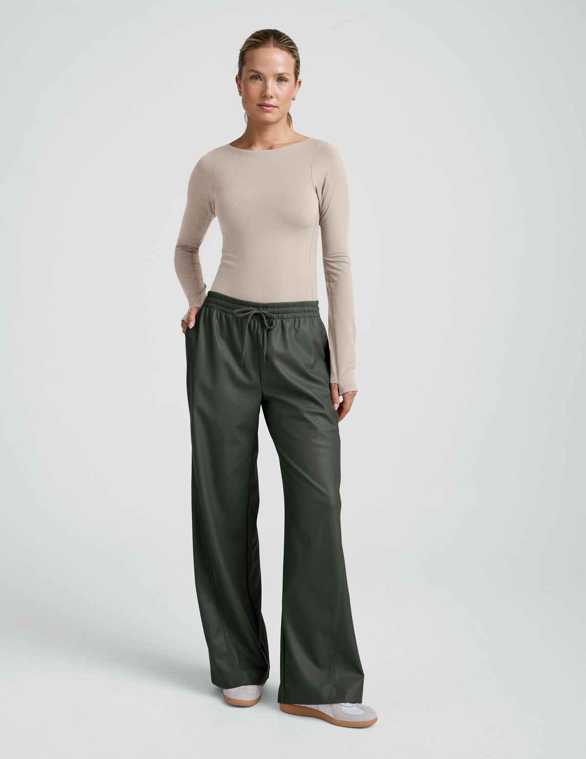 woman wearing a neutral color long sleeve bodysuit and green faux leather pants.