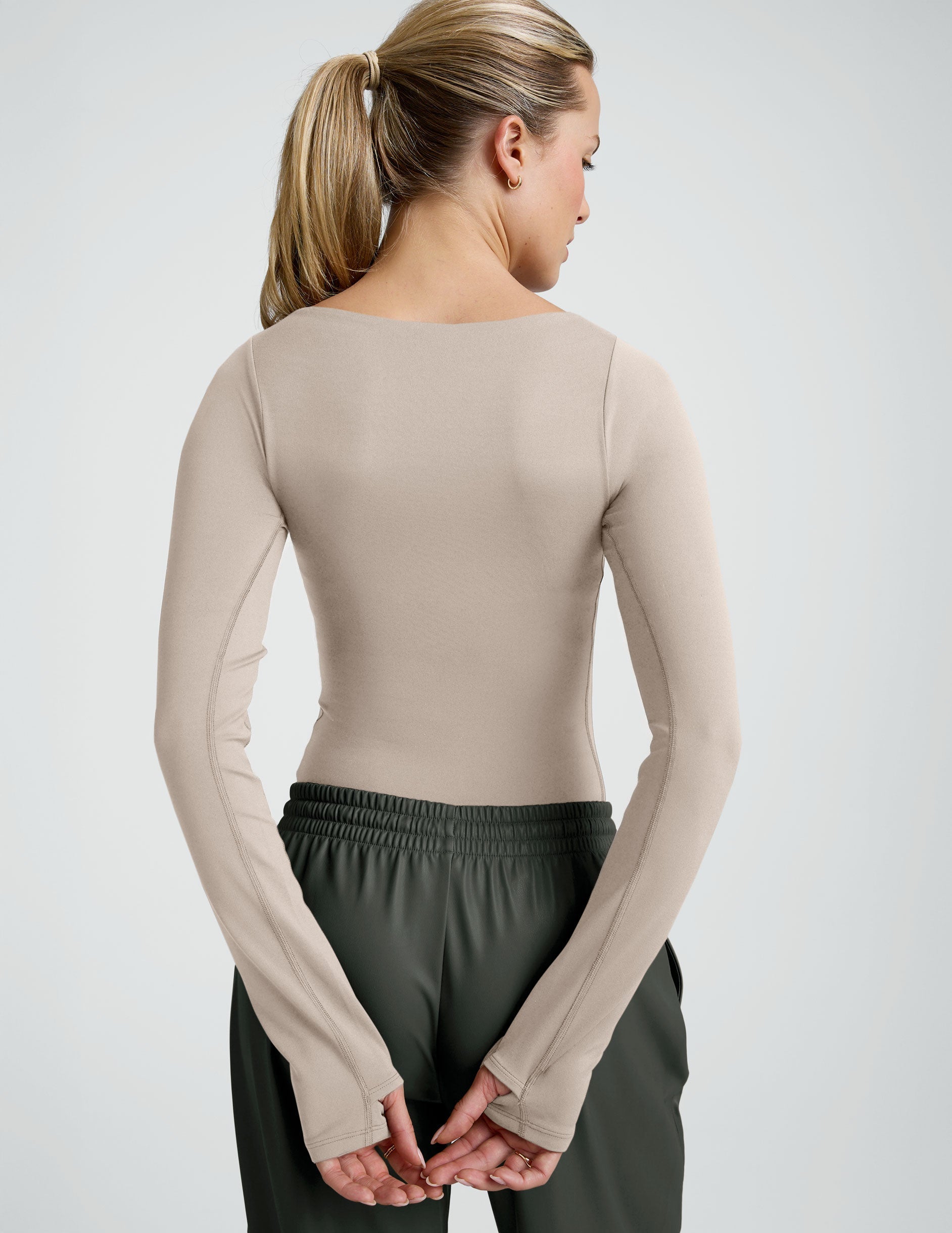 woman wearing a neutral color long sleeve bodysuit and green faux leather pants.