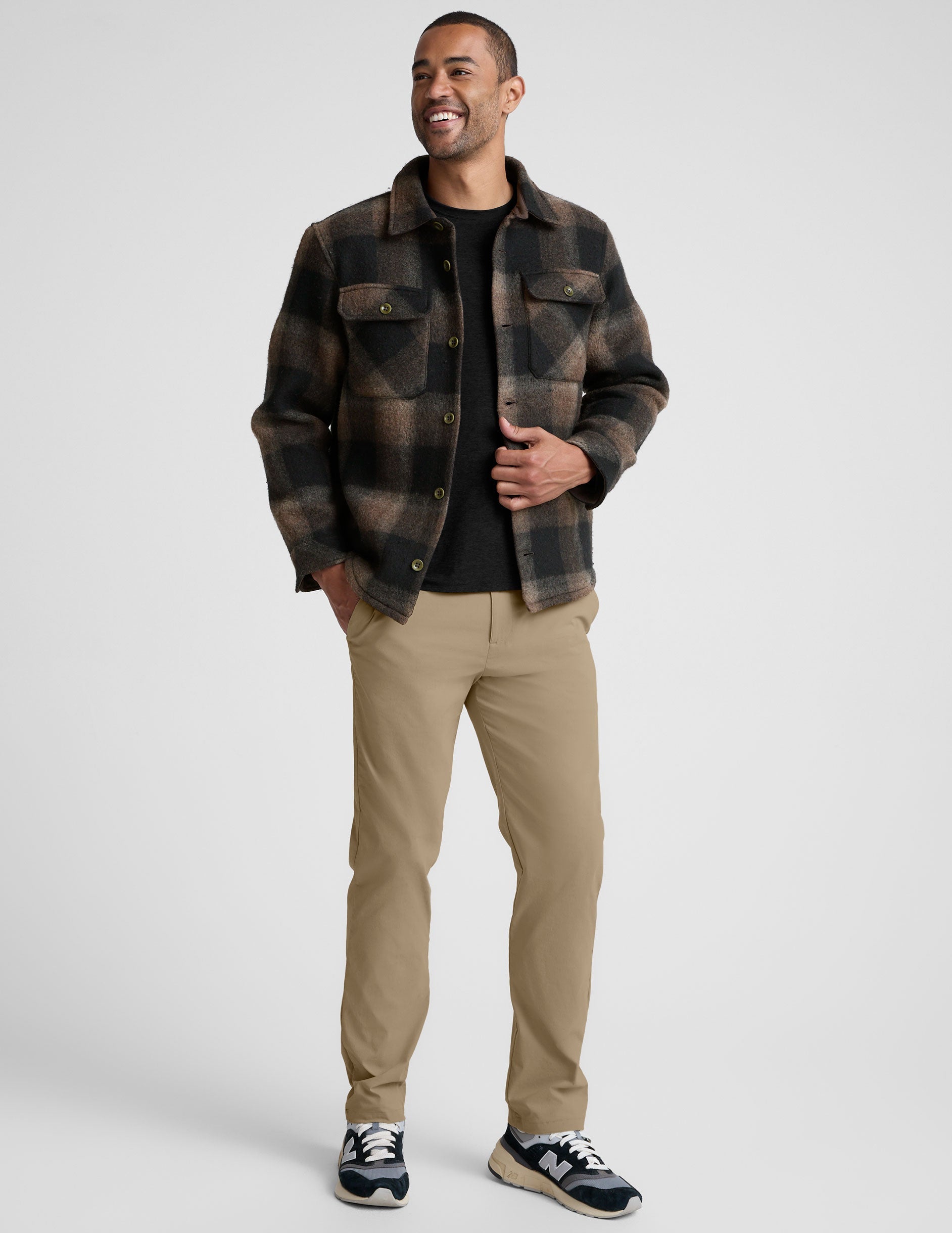model wearing a men's plaid button-up jacket over a black shirt on a light gray background.