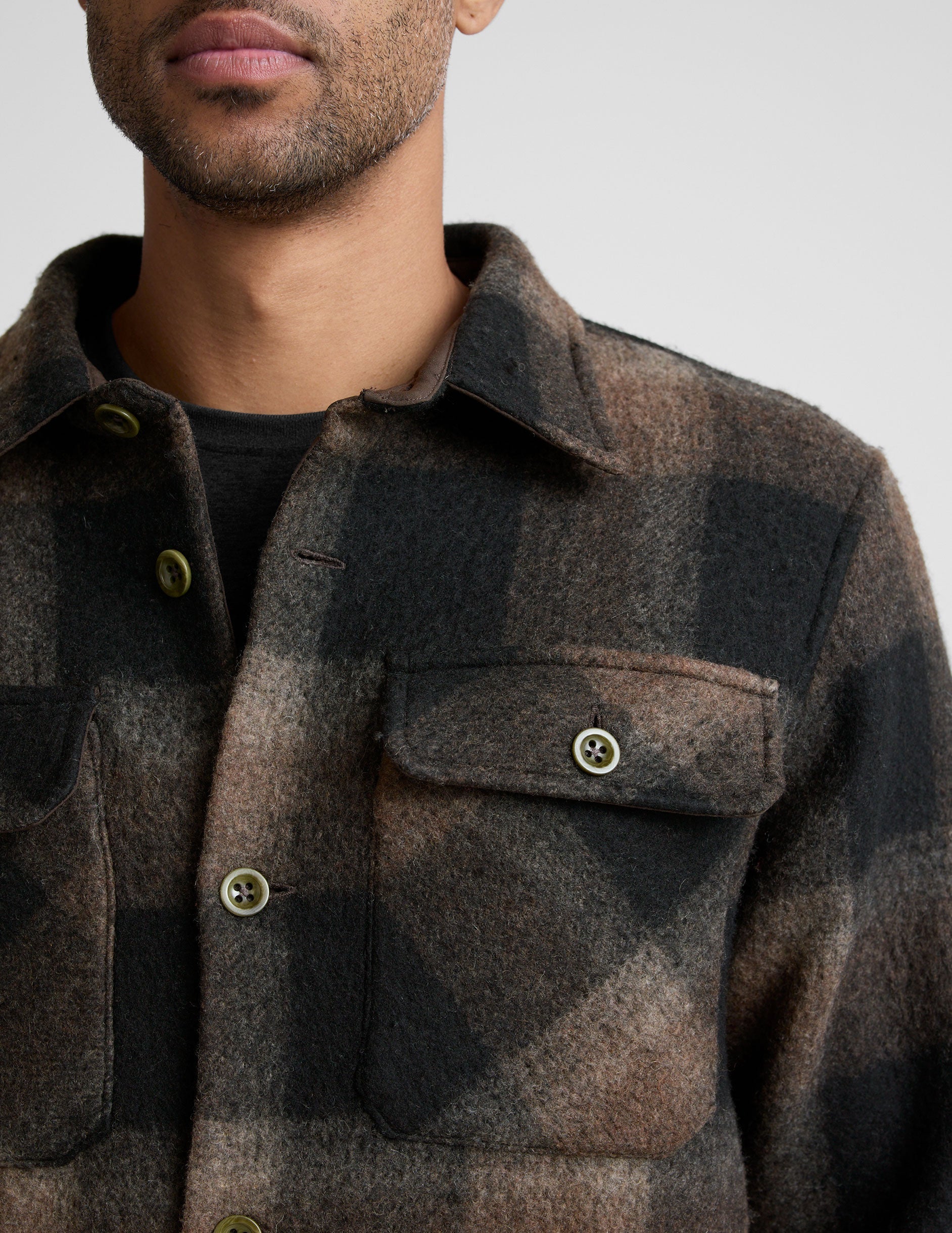 model wearing a men's plaid button-up jacket over a black shirt on a light gray background.