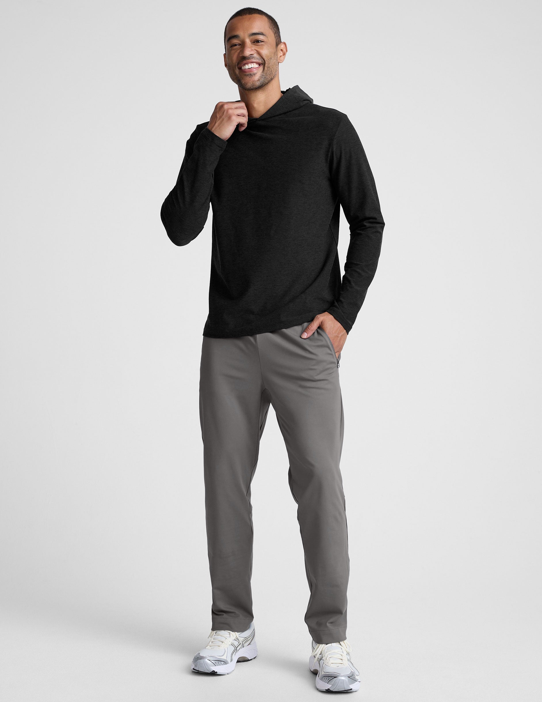 man wearing a black hoodie and gray pants on a white background.