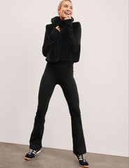 person wearing a black faux fur vest and black fleece lined pants against a plain background.