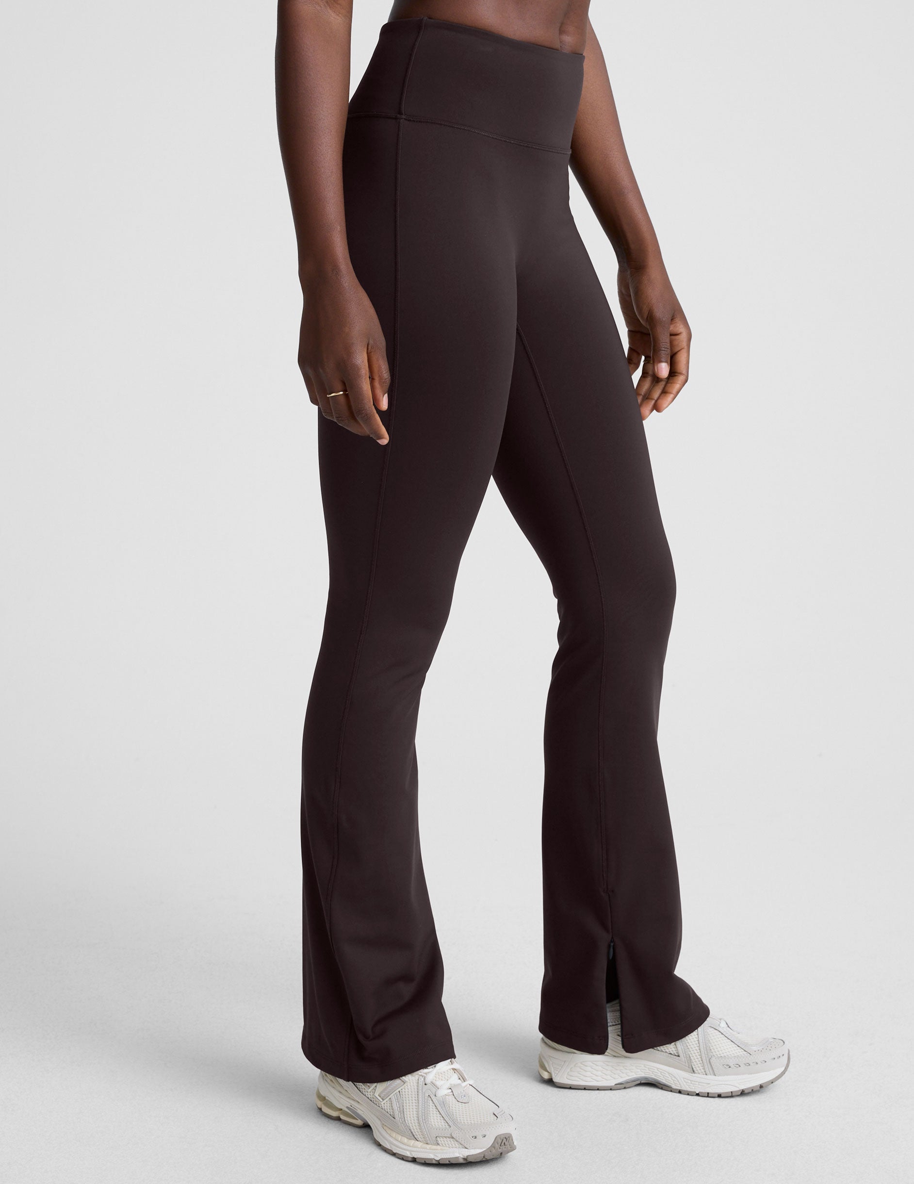 woman wearing a brown sleeveless top and pants on a white background.