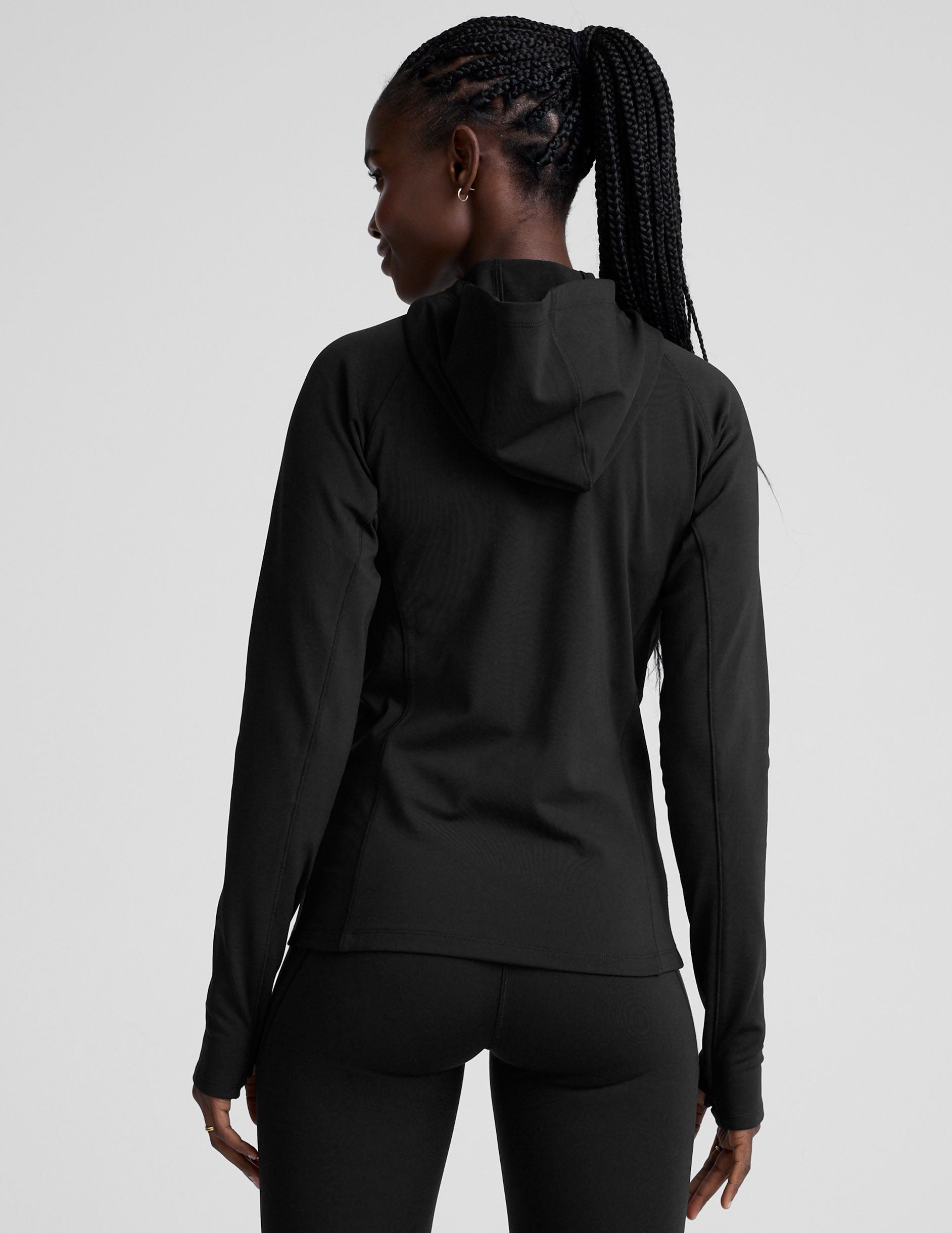 woman in black zip-up hooded jacket and leggings against a plain background.