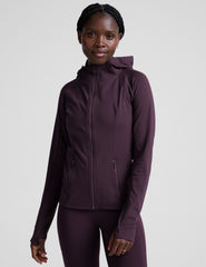 woman wearing a purple hooded jacket and leggings on a plain background.