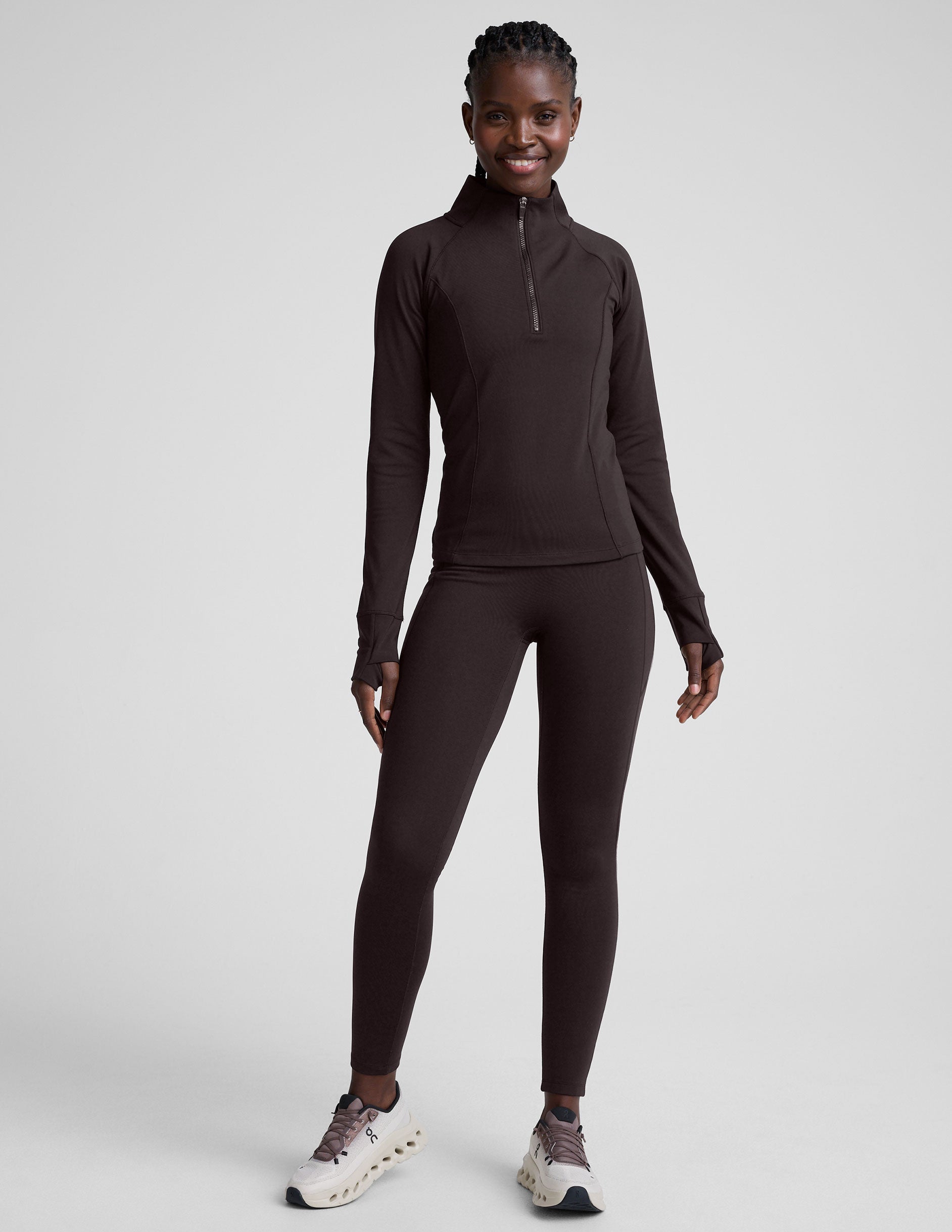 person wearing brown high-waisted long leggings with pockets on a plain background.