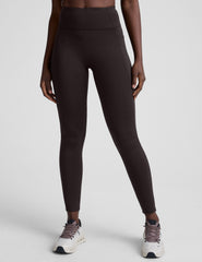 person wearing brown high-waisted long leggings with pockets on a plain background.