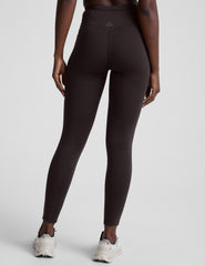 person wearing brown high-waisted long leggings with pockets on a plain background.