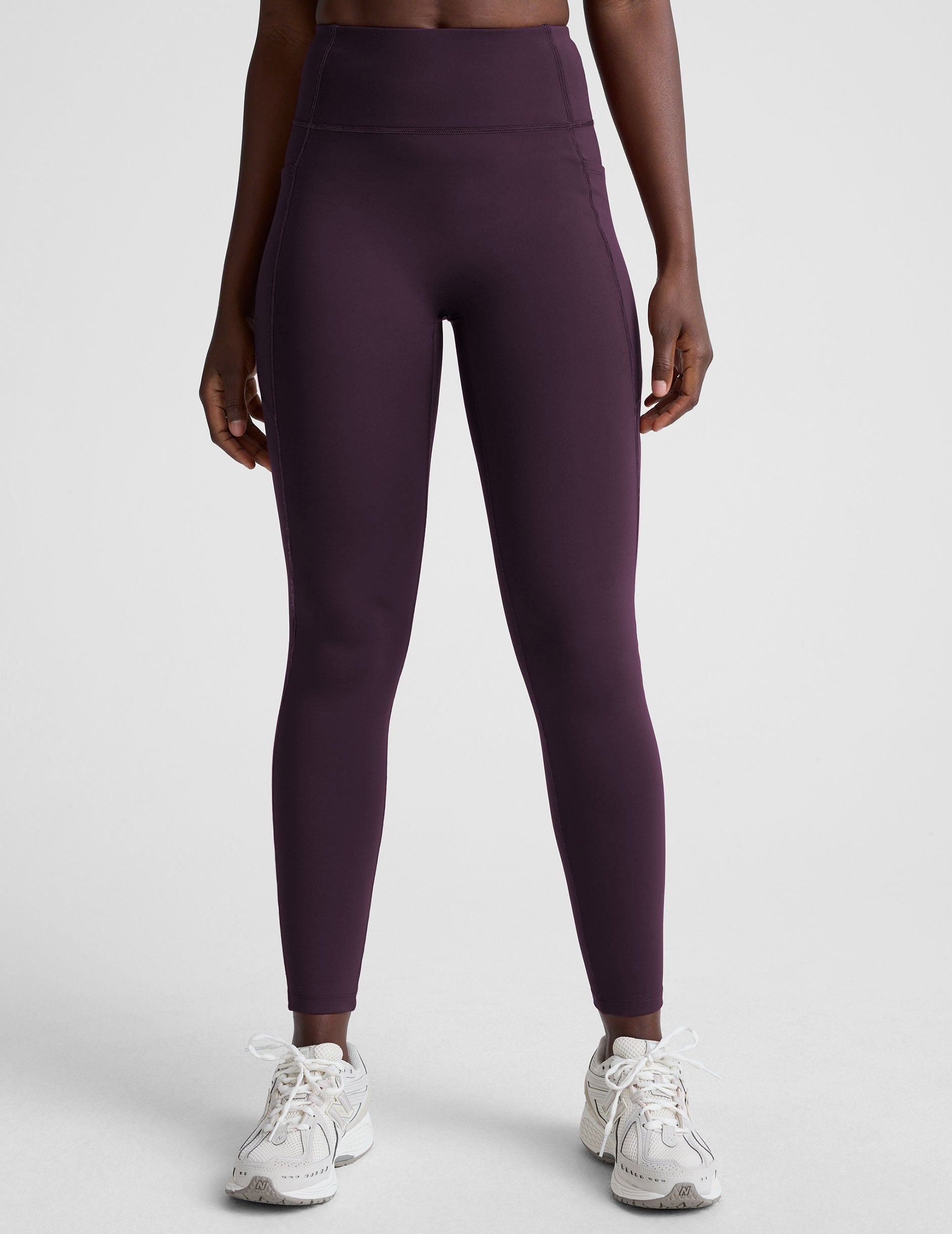woman wearing high-waisted purple long length leggings with pockets against a plain background.