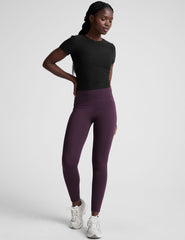 woman wearing a black t-shirt and purple leggings on a plain background.