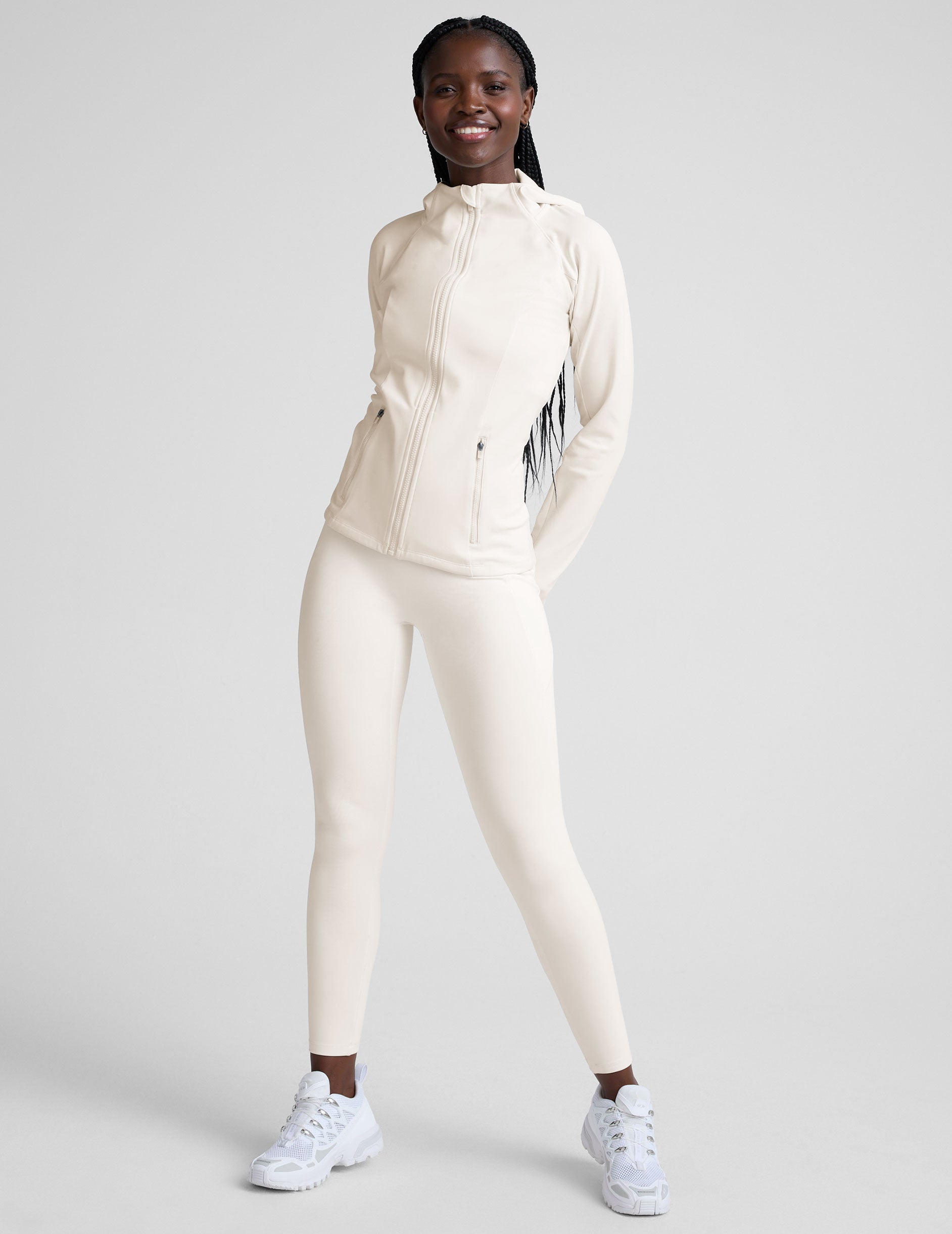 woman wearing white high-waisted long length leggings with pockets on a plain background.