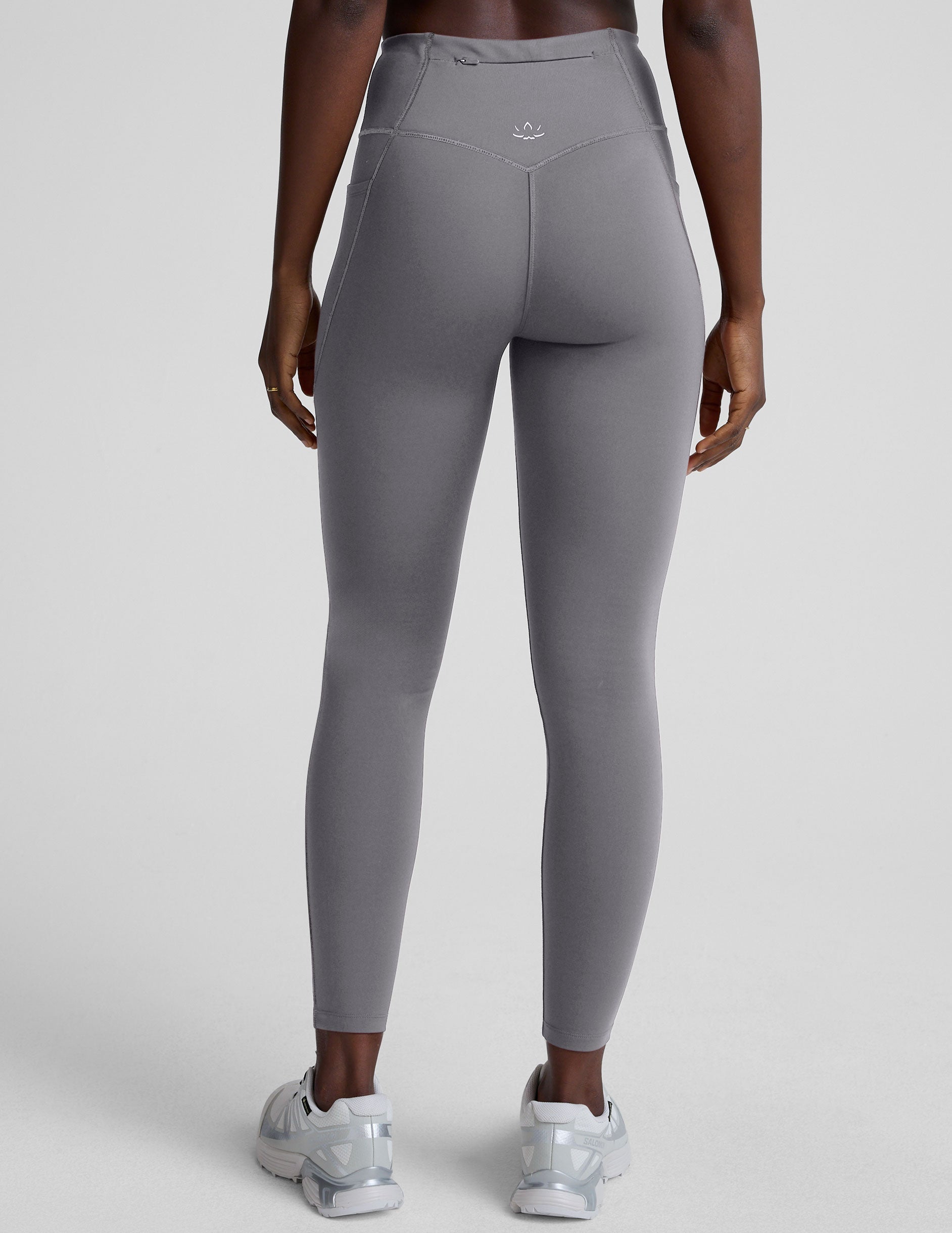 woman wearing gray high-waisted long length leggings on a plain background.