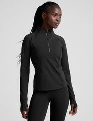 woman wearing a black long-sleeve athletic jacket with a zipper on a plain background.