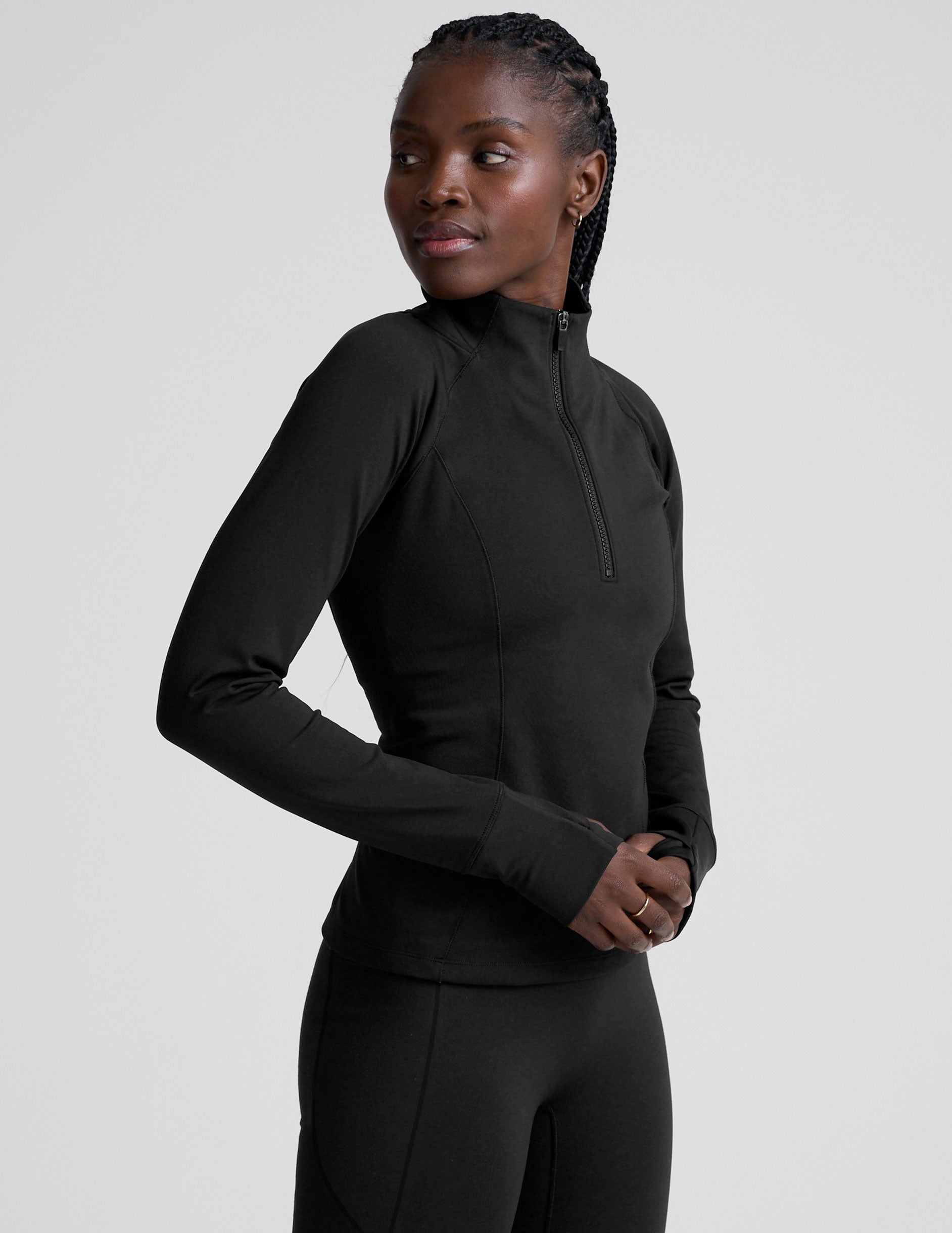 woman wearing a black long-sleeve athletic jacket with a zipper on a plain background.