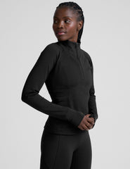 woman wearing a black long-sleeve athletic jacket with a zipper on a plain background.