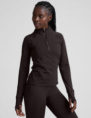 woman wearing a brown quarter-zip jacket and leggings on a plain background.