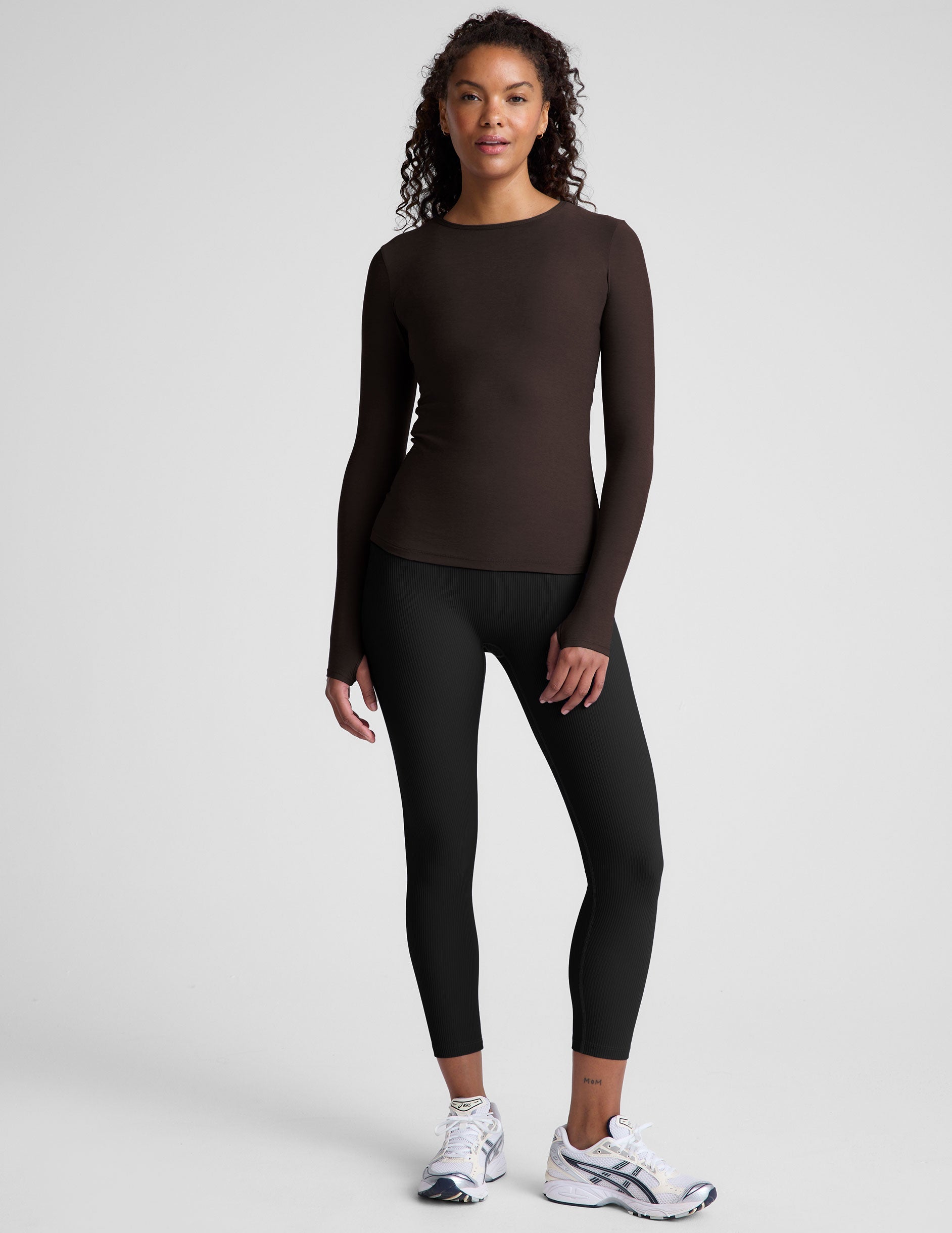 Woman wearing a brown long-sleeve top and black leggings on a plain background.