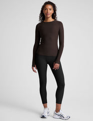 Woman wearing a brown long-sleeve top and black leggings on a plain background.