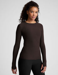 Woman wearing a brown long-sleeve top and black leggings on a plain background.