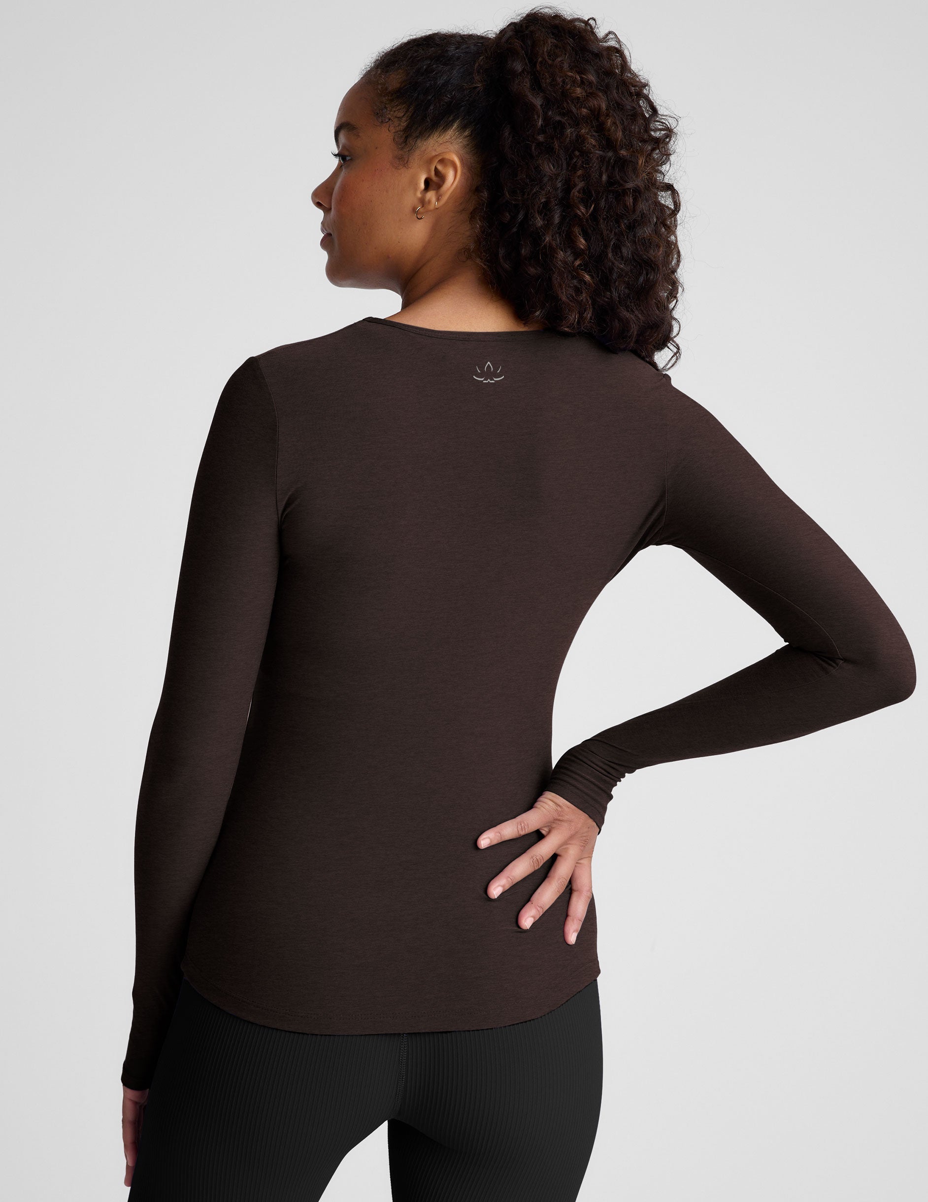 Woman wearing a brown long-sleeve top and black leggings on a plain background.