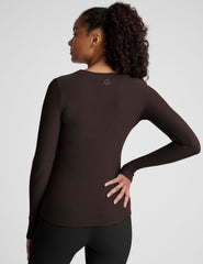 Woman wearing a brown long-sleeve top and black leggings on a plain background.