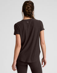 woman wearing a brown t-shirt and leggings on a light gray background.
