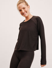 woman wearing a brown long-sleeve top and leggings on a plain background.