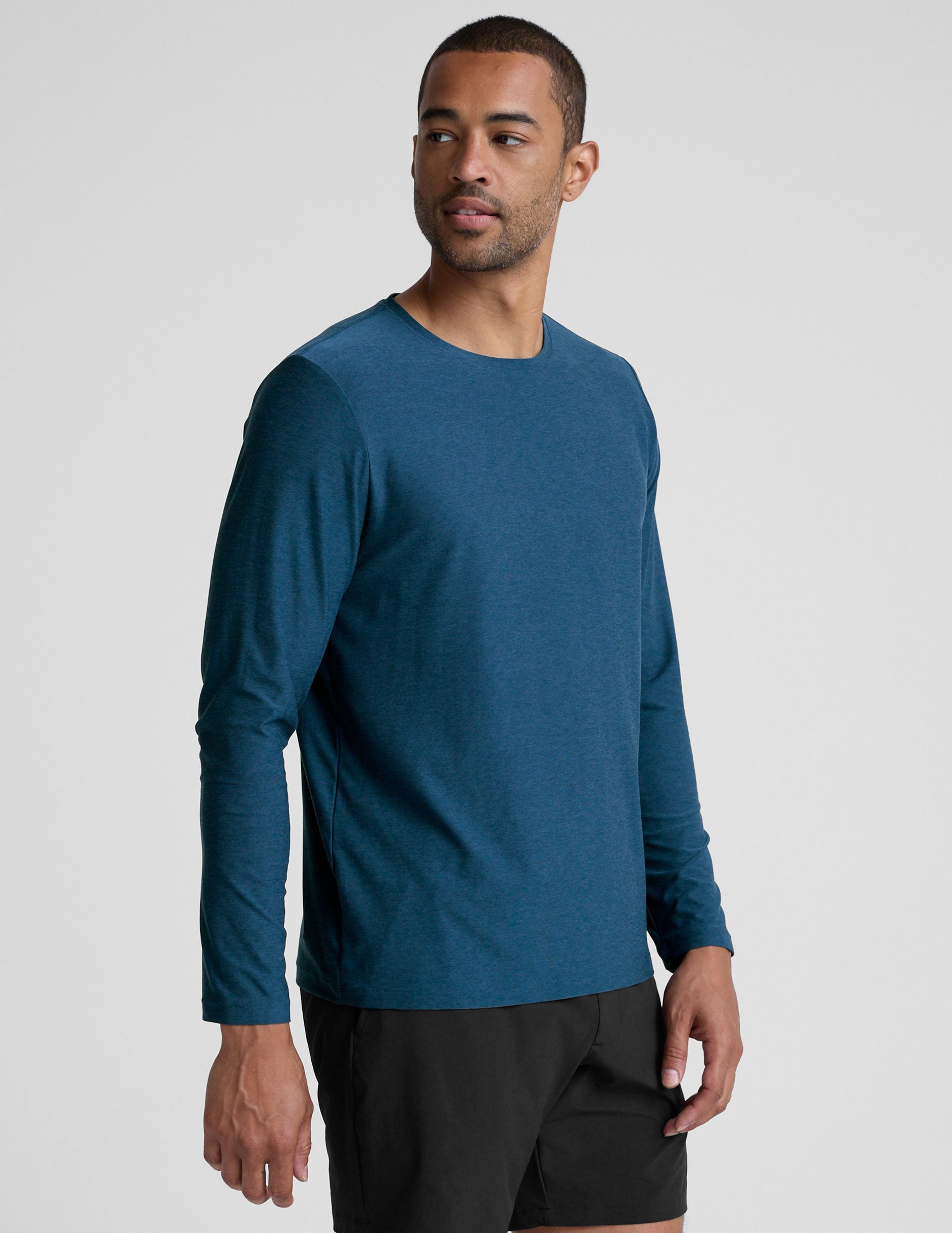 man wearing a blue long-sleeve shirt and black shorts against a gray background.