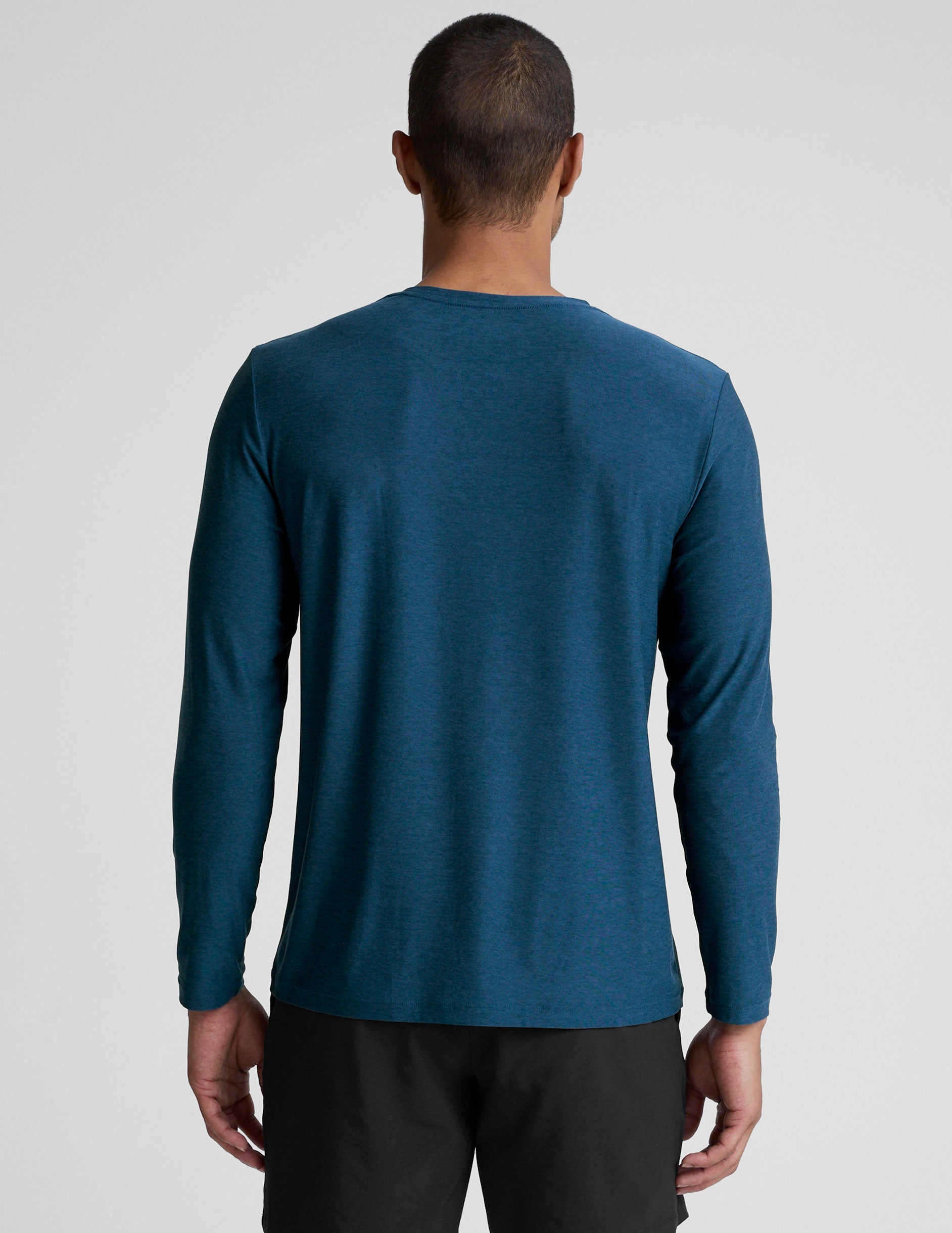 man wearing a blue long-sleeve shirt and black shorts against a gray background.