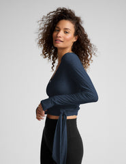Woman wearing a blue long-sleeve wrap top and black leggings on a plain background.