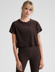 woman wearing a brown cropped t-shirt and leggings on a plain background.