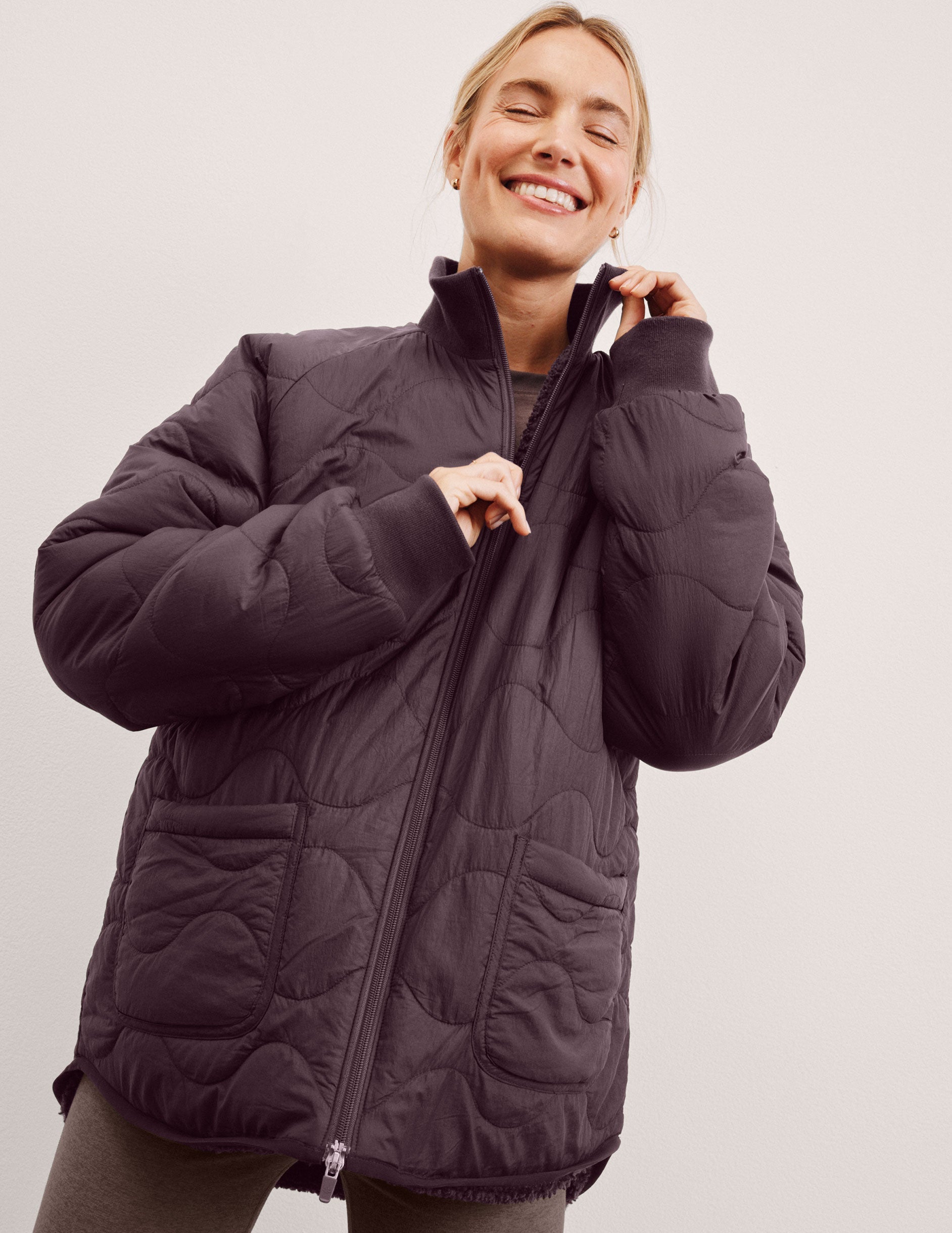 woman wearing a purple quilted jacket against a plain background.