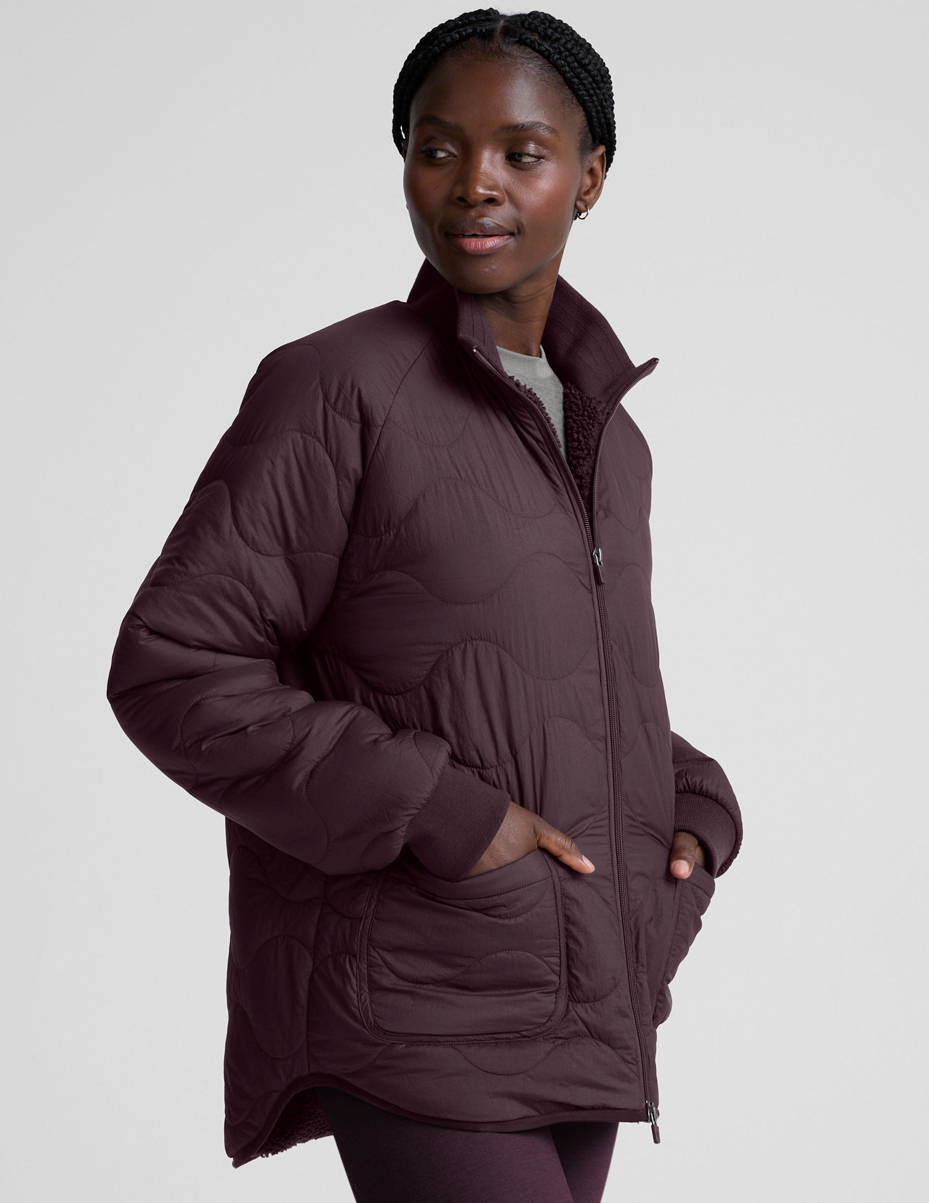 woman wearing a purple quilted jacket against a plain background.