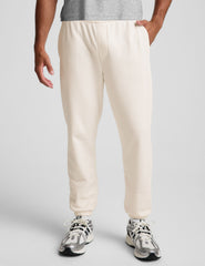man wearing a gray crew neck t-shirt and white fleece sweatpants on a plain background.