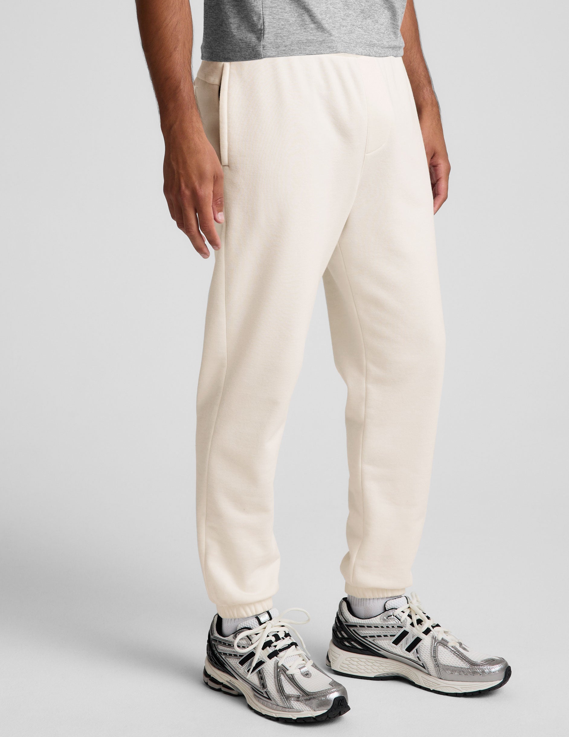 man wearing a gray crew neck t-shirt and white fleece sweatpants on a plain background.