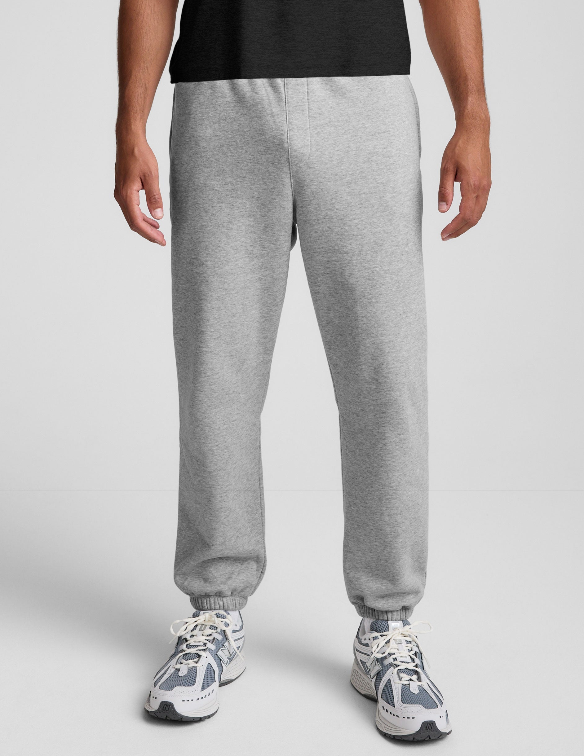 man wearing a black crew neck t-shirt and gray fleece sweatpants on a light gray background.