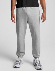 man wearing a black crew neck t-shirt and gray fleece sweatpants on a light gray background.