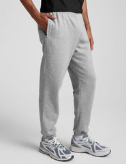 man wearing a black crew neck t-shirt and gray fleece sweatpants on a light gray background.