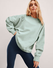 woman wearing a light blue sweatshirt and dark blue leggings against a plain background.
