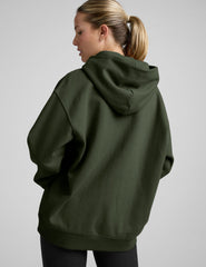 woman wearing a green oversized hoodie and black leggings on a gray background.