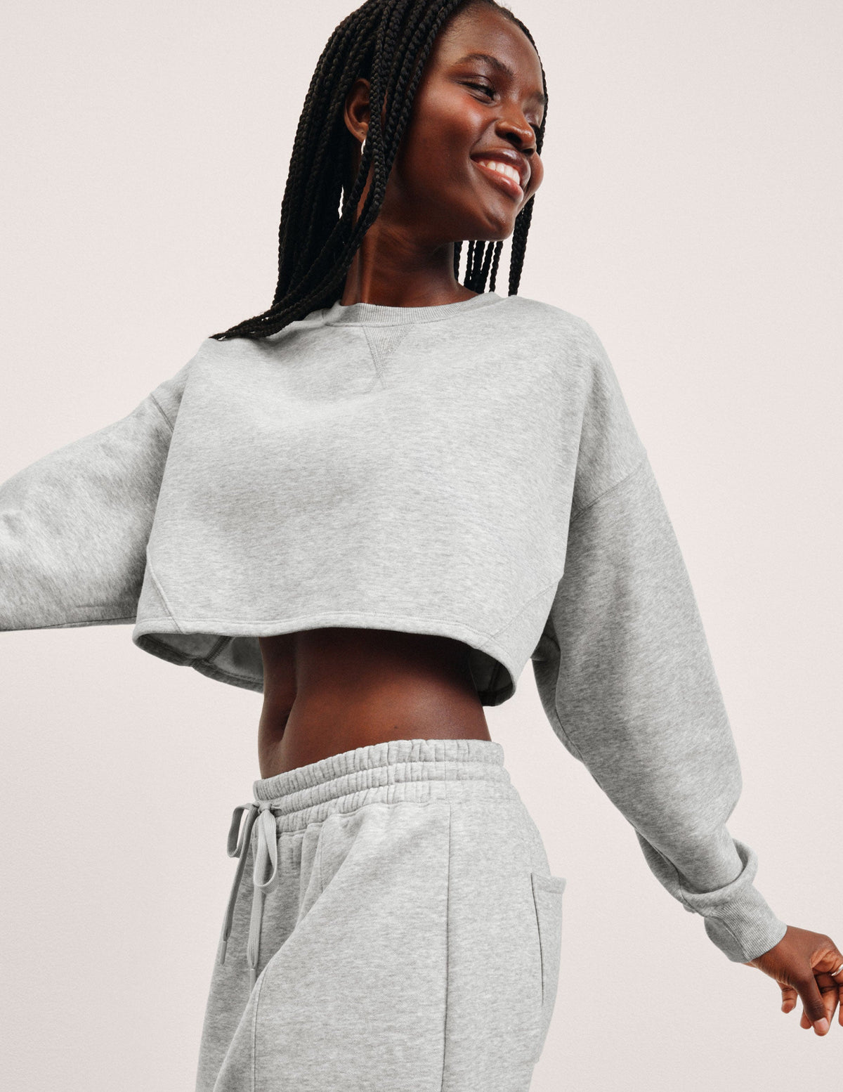 woman wearing a gray cropped sweatshirt and matching barrel fleece pants on a plain background.