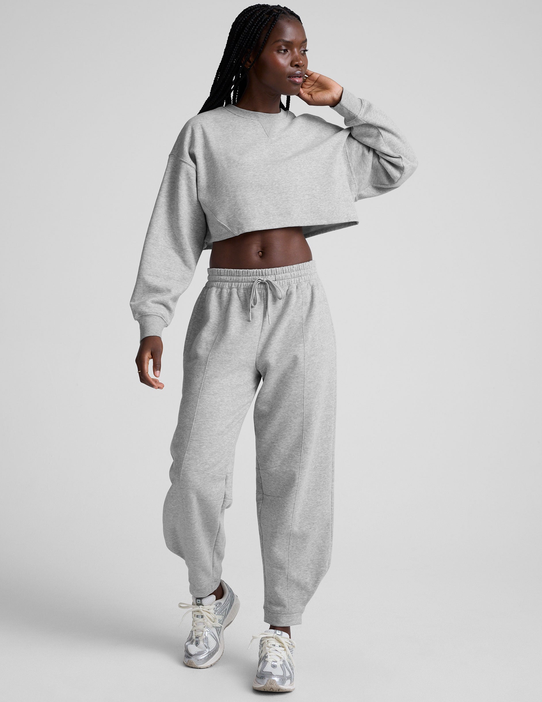 woman wearing a gray cropped sweatshirt and matching barrel fleece pants on a plain background.