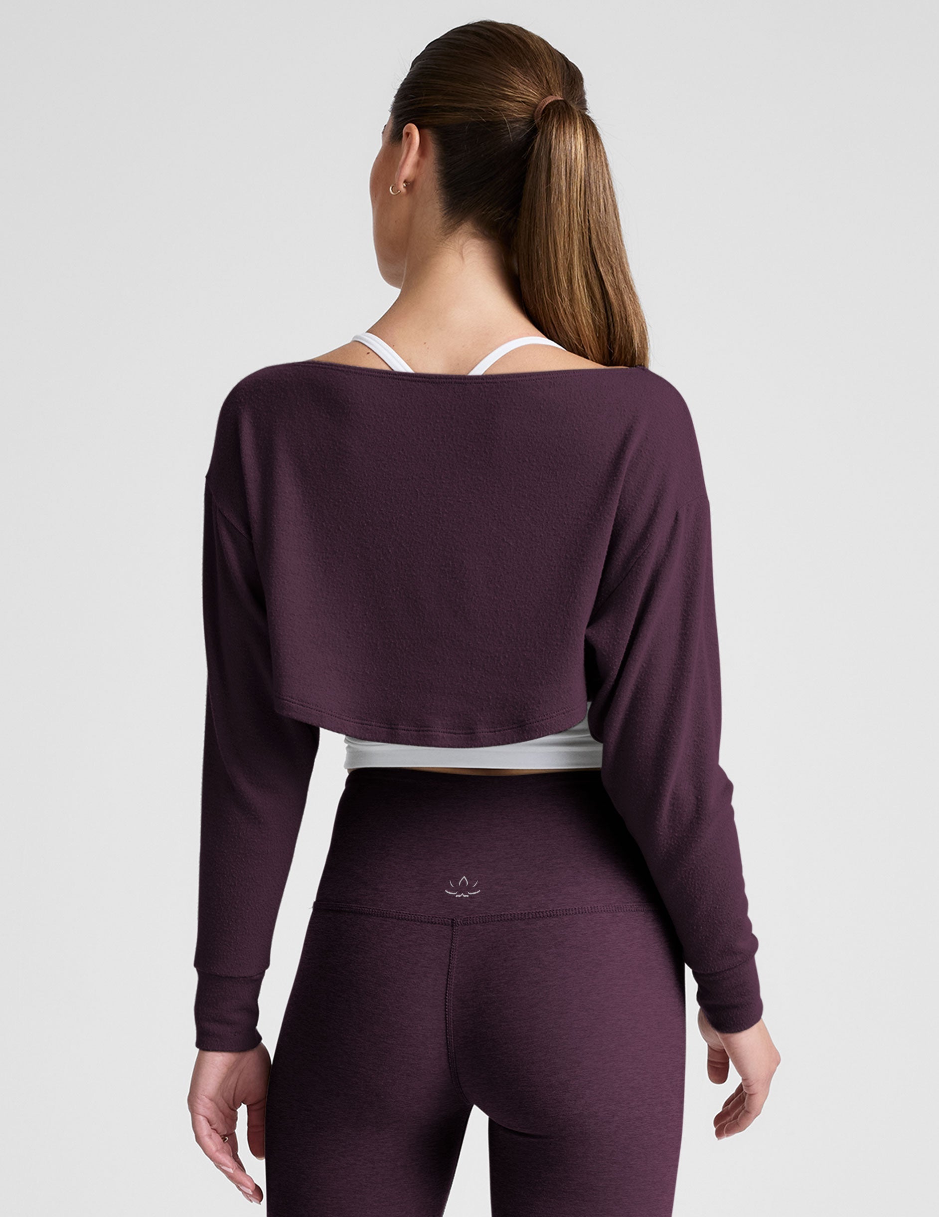 model wearing a white cropped tank and purple leggings with a purple shrug on a light background.