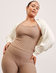 woman wearing a beige top and pants with a white shrug on a plain background.